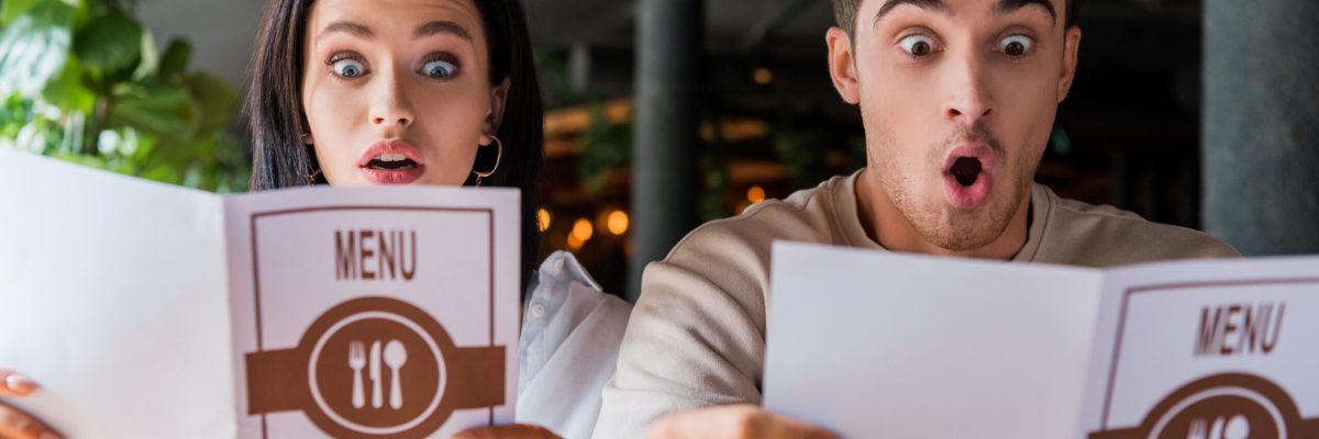 shocked man and woman looking at menus in restaurant